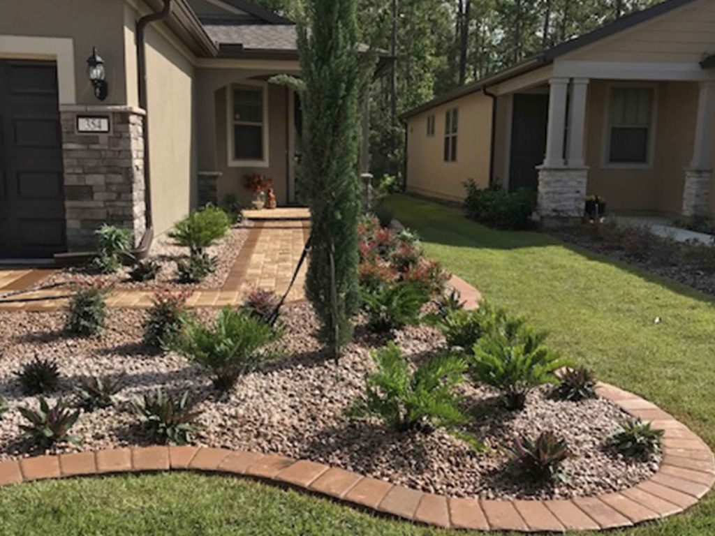 Updated entry with bright rock edging, stones, cedar, and plants.